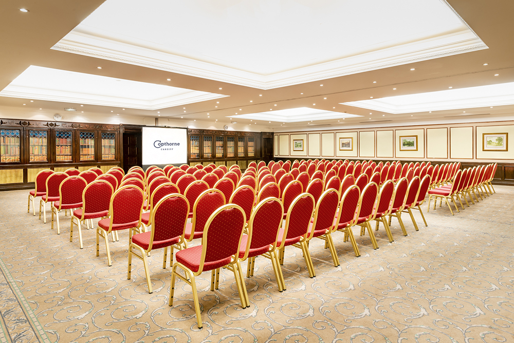 Large room in the Copthone hotel set up for a talk, with rows of chairs facing a large screen