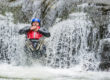 A man wearing a wetsuit, hard hat and buoyancy aid slides down a waterfall