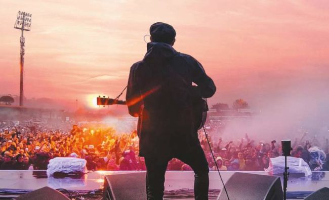 Gerry Cinnamon from the back on stage in front of a crowd in the evening