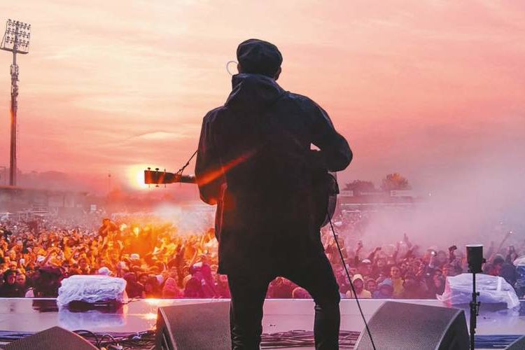 Gerry Cinnamon from the back on stage in front of a crowd in the evening